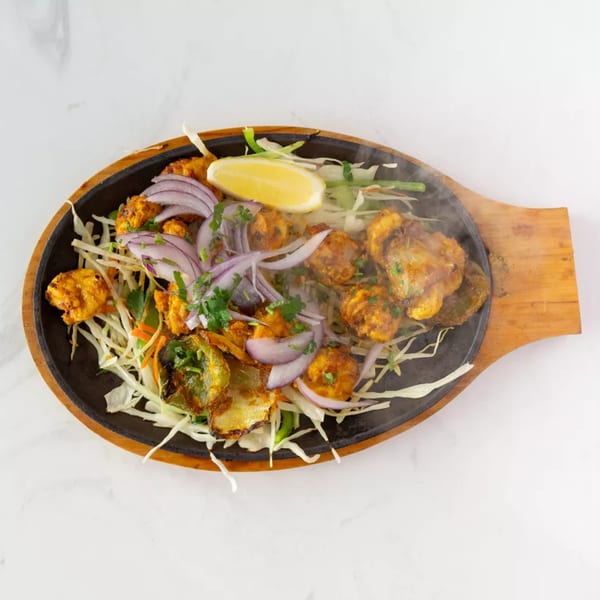 Sizzling chicken tikka with onions, peppers, and lemon on a hot platter.