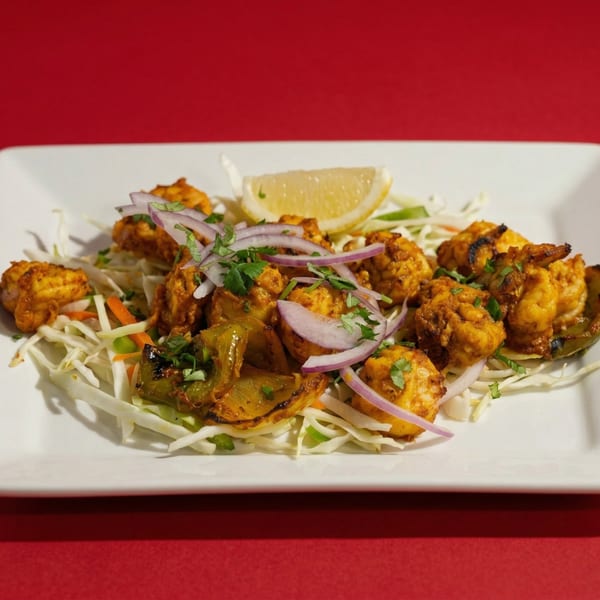 Grilled chicken tikka with bell peppers, red onions, cilantro, and a lemon wedge on shredded cabbage.