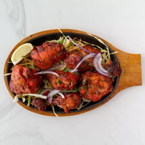 Tandoori chicken pieces with sliced red onions and lemon on a sizzling platter.