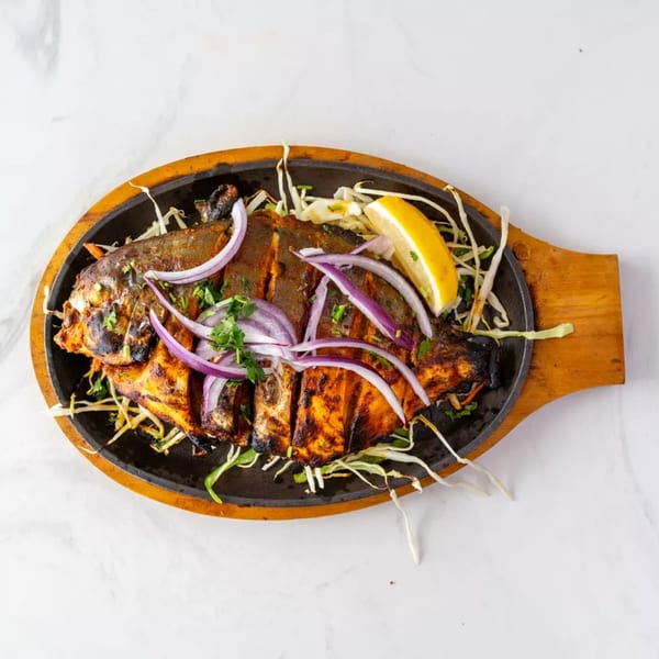Grilled whole fish, garnished with red onions, cilantro, and a lemon wedge, served on a sizzling platter.